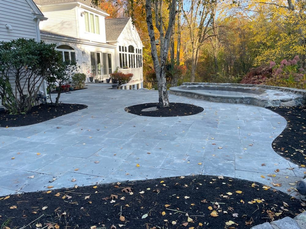 Patio with stone paving, fire pit, and autumn foliage in a residential backyard setting.