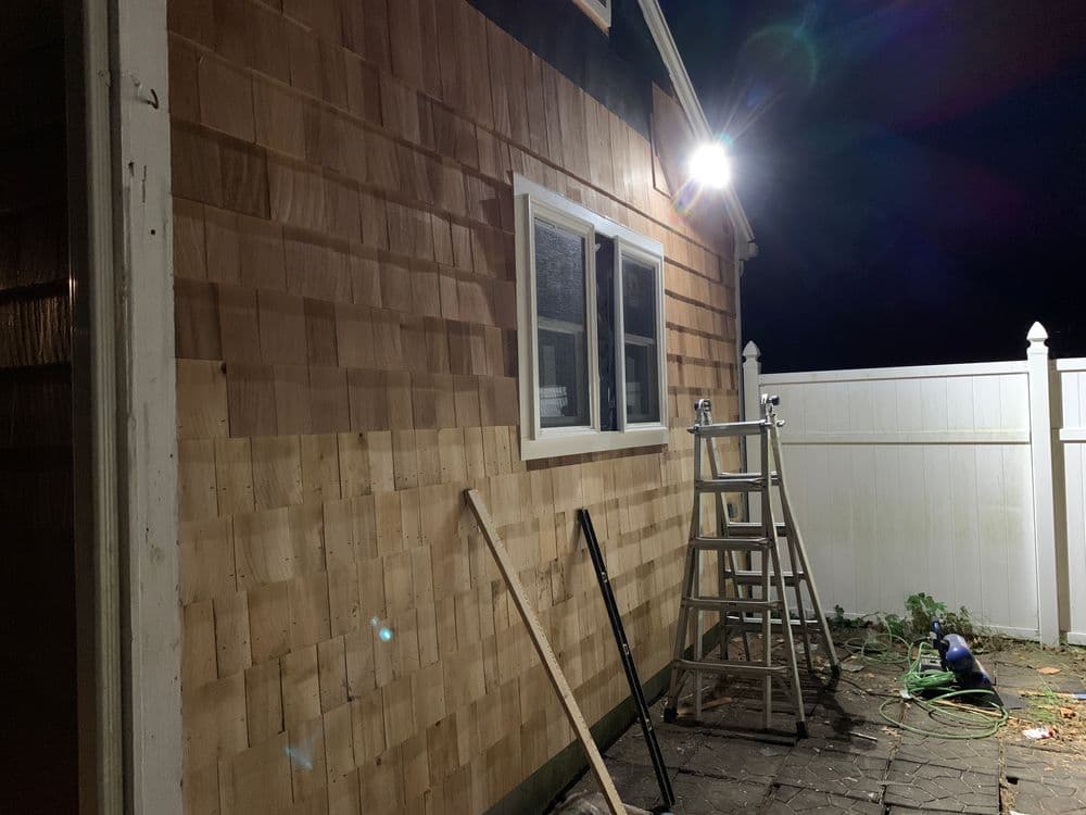 Nighttime view of a wooden house exterior under renovation, featuring a ladder and tools.