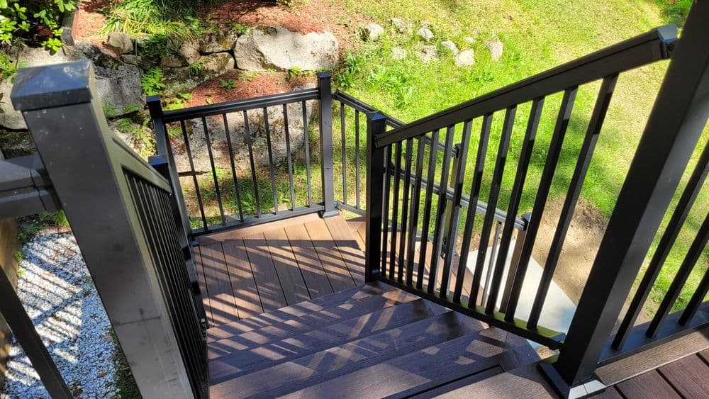 Black metal railing staircase leading down to a lush green garden, showcasing wooden steps.