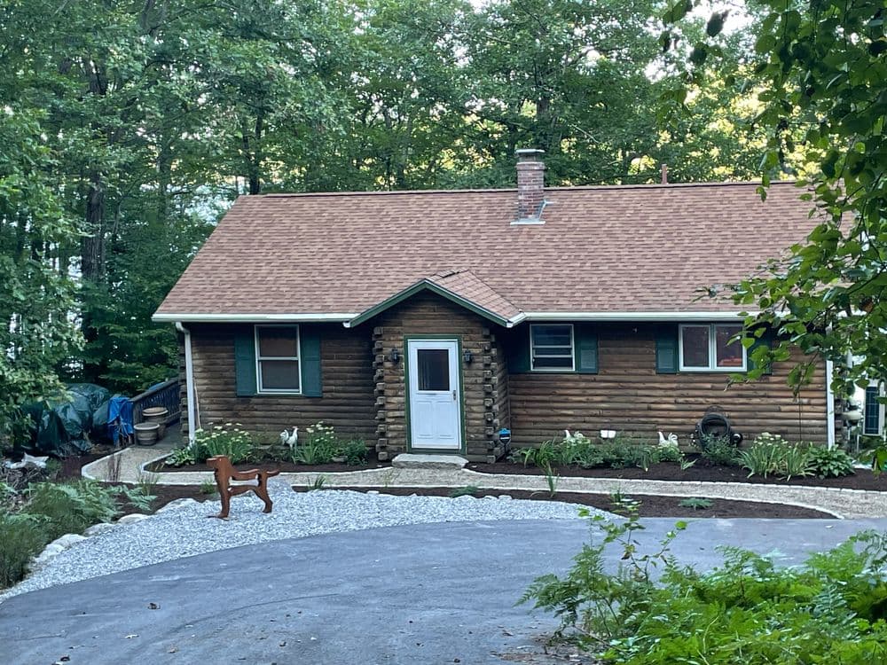 Log cabin home surrounded by trees with a gravel driveway and landscaped garden.