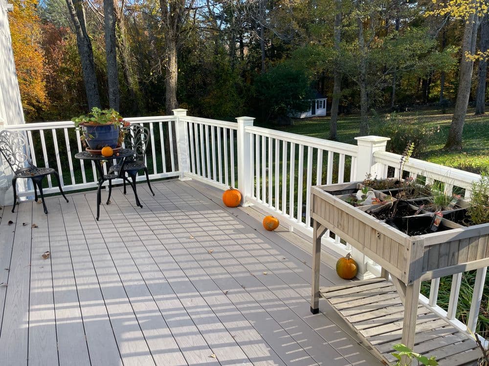 Cozy autumn deck with pumpkins, a planter, and chairs surrounded by colorful fall foliage.