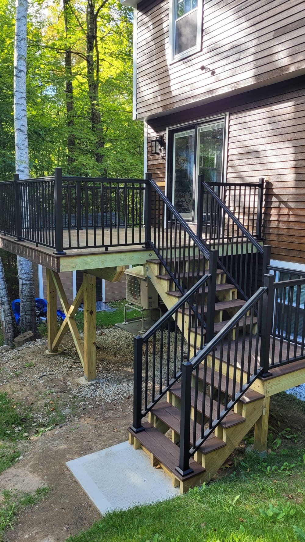 Modern outdoor wooden deck with black railings and stairs, surrounded by trees.