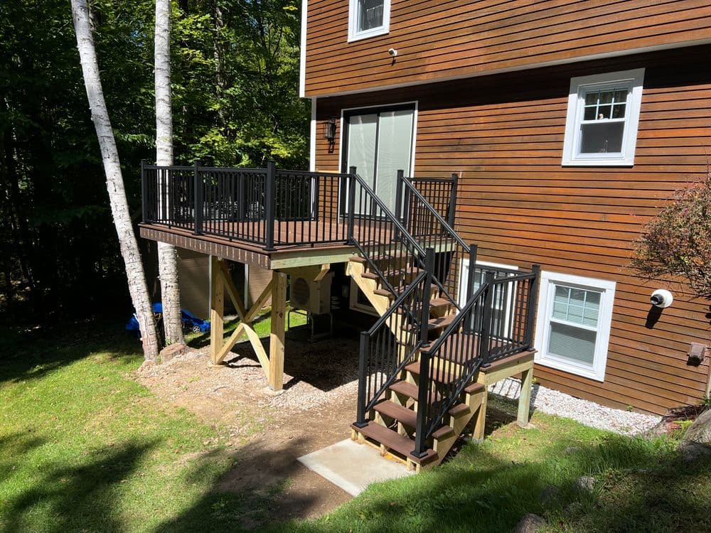 Home exterior with a wooden deck and black railing, featuring stairs and green lawn area.