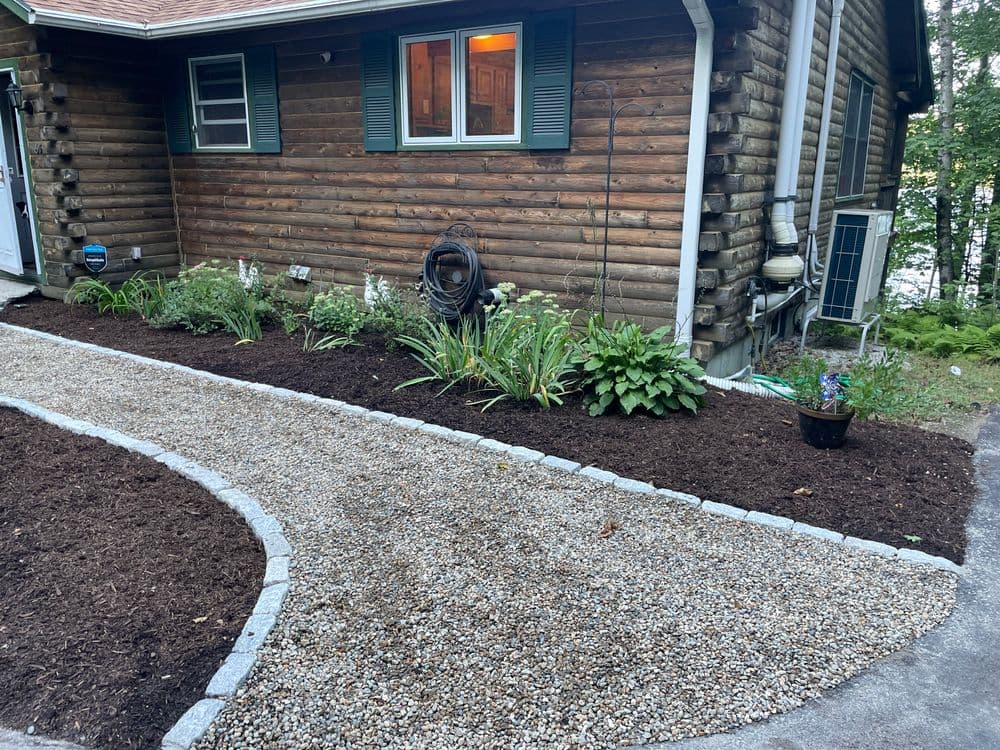 Updated home's landscaping with gravel path, mulched flower beds, and greenery.