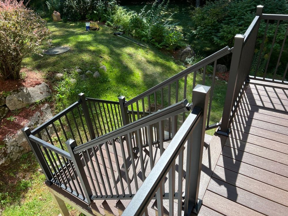 Black metal outdoor stairs leading to a landscaped backyard with greenery and stones.