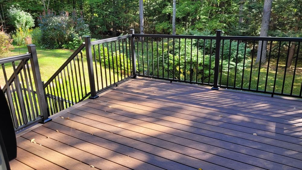 Spacious backyard deck with black railing surrounded by greenery. Perfect for outdoor living.