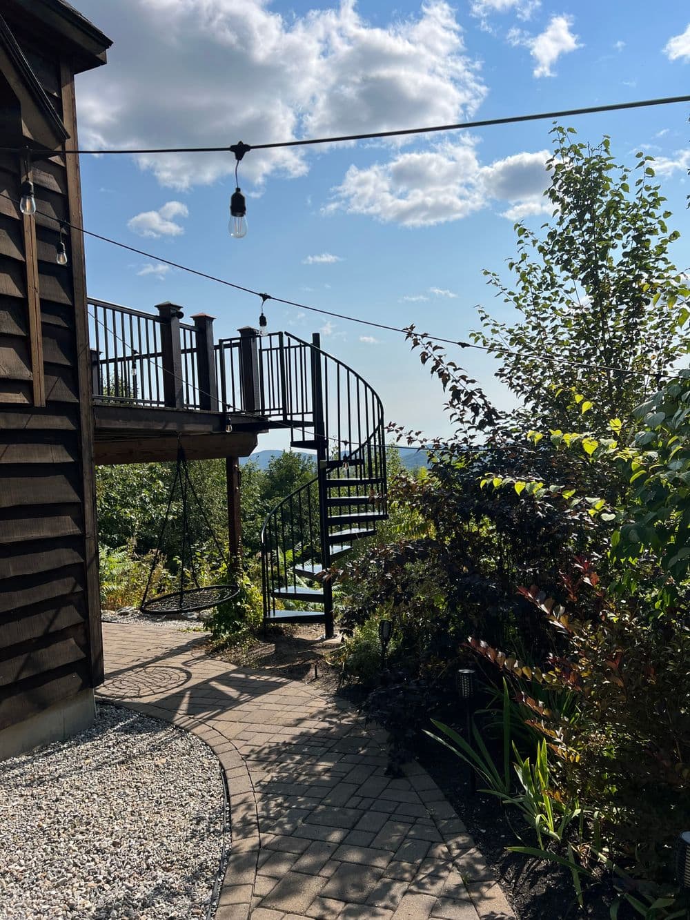 Spiral staircase leads to a deck with scenic views, surrounded by lush greenery and bright skies.