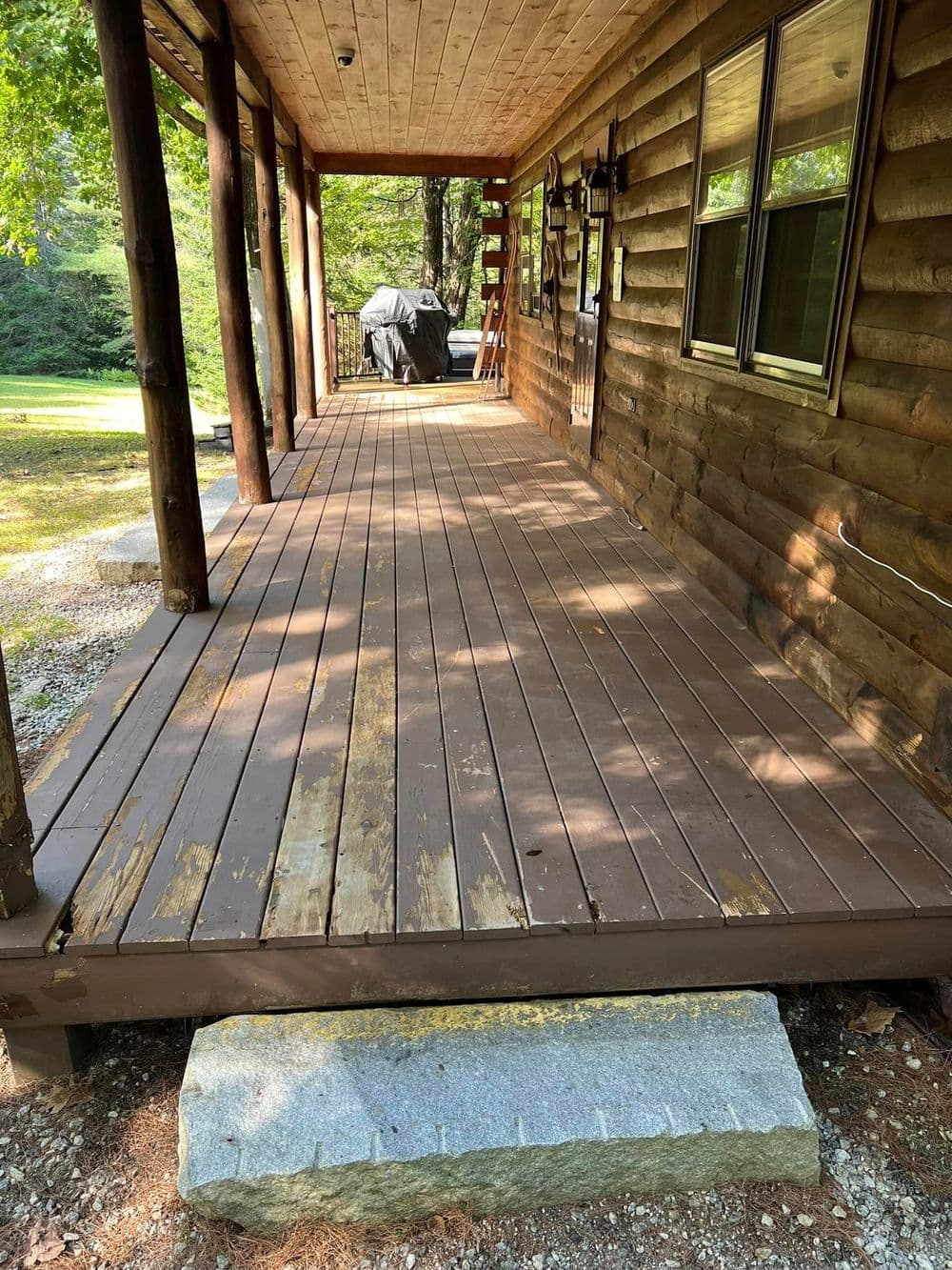 Wooden porch of a cabin with a grill and natural surroundings, featuring stained wood planks.
