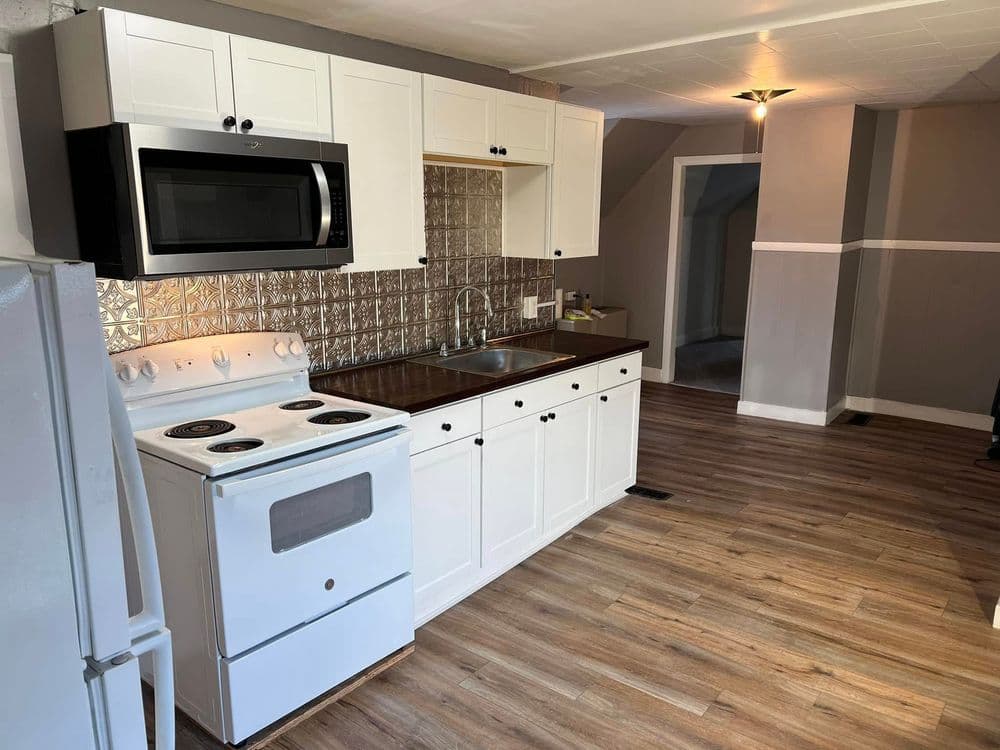 Modern kitchen featuring white cabinets, stainless steel backsplash, and built-in microwave.