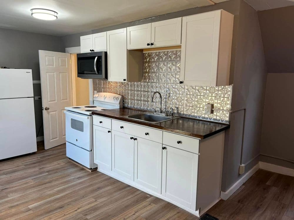 Modern kitchen with white cabinets, stainless steel sink, and patterned backsplash.
