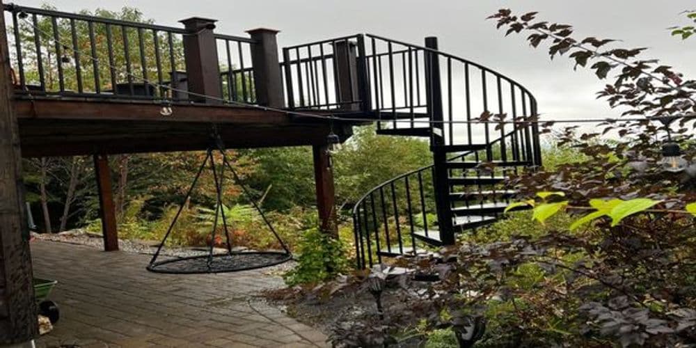 Spiral staircase leading to a deck surrounded by lush greenery and a swing.